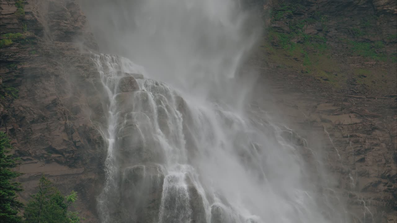 Tilt down shot of a waterfall going down rugged rock formations, sending mist and spray into the air, close up shot