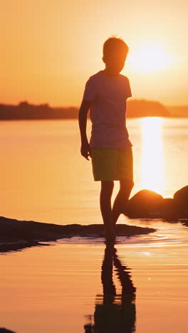 boy plays near the water. silhouette of boy near stones area in water vertical video