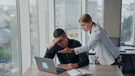 confused man having some troubles in work. man looks at his laptop and female colleague trying to help. lady turns around and leaves annoyed.