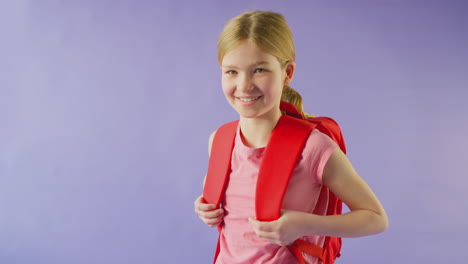 Studio-Shot-Of-Girl-With-Backpack-Going-To-School-On-Purple-Background