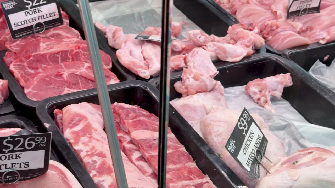 Various cuts of beef and pork displayed in a well-lit butcher shop, slow camera pan