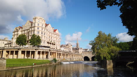 static shot of the empire hotel, pulteney weir - pulteney bridge in bath, somerset on beautiful summer’s morning with blue sky and golden light