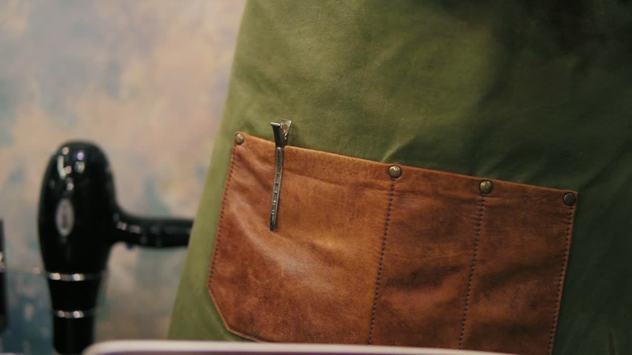Close Up view of male barber's hands placing hair pins or barrette to the pocket in his apron while preparing for a haircut