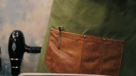 close up view of male barber's hands placing hair pins or barrette to the pocket in his apron while preparing for a haircut