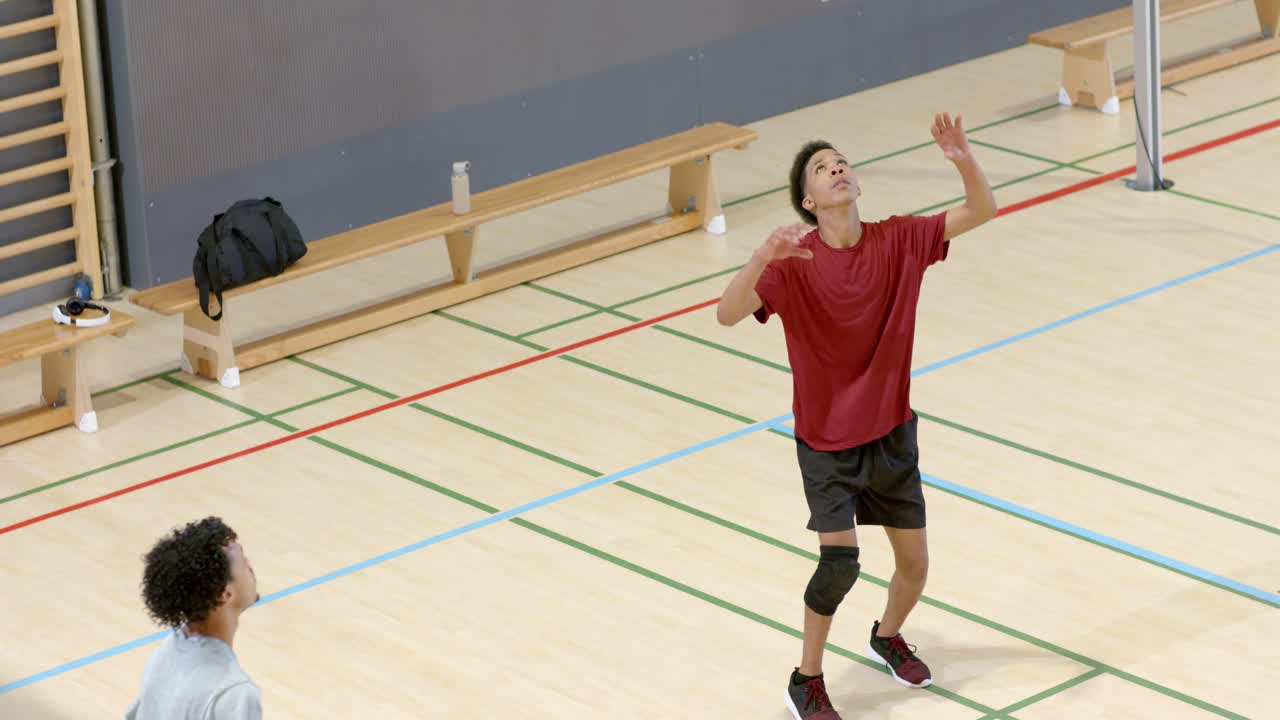 Alzatore di pallavolo maschile in maglietta rossa che segue il lancio, eseguendo un palleggio in elevazione sopra la rete durante un'esercitazione in palestra.