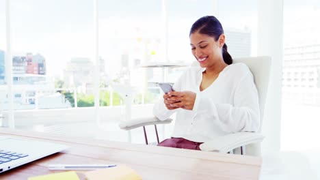 Mujer-Sonriente-Usando-Un-Teléfono-Inteligente-En-La-Oficina