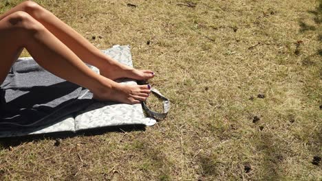 feet are resting on a towel placed on dry grass under the bright sunshine, creating a relaxed atmosphere perfect for enjoying a warm afternoon outdoors