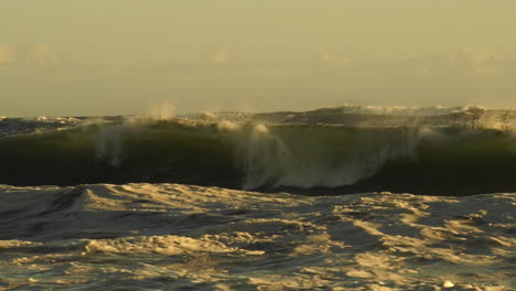 Olas-Del-Mar-Agitadas-Rompiendo-En-La-Costa-Rocosa-Creando-Un-Enorme-Rocío-Durante-La-Puesta-De-Sol-Dorada---Plano-Medio