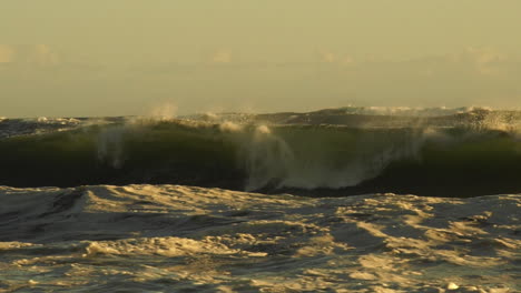 las olas violentas del mar chocan contra la costa rocosa creando un gran chorro durante la puesta de sol dorada.