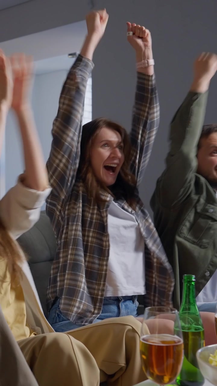 Glade venner jubler og fejrer, mens de ser tv derhjemme.