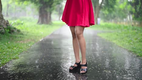 sexy wet legs and feet of a beautiful girl standing on a road in rain, slow motion, short pinkish red dress