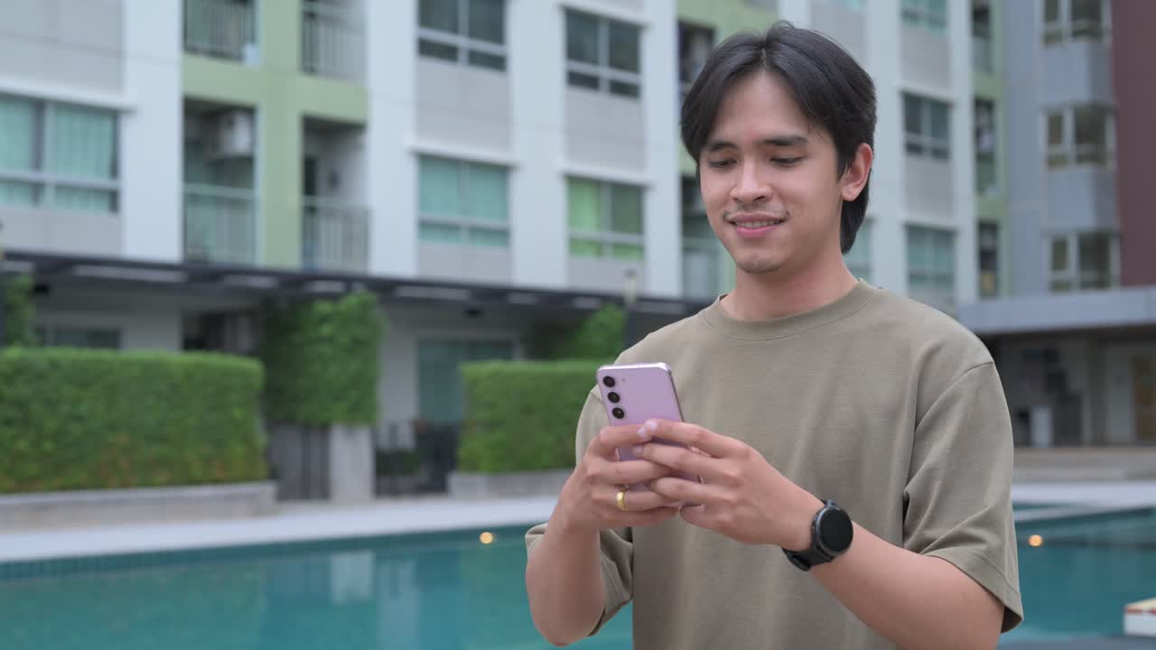Handsome young Asian Thai man in early 20s smiling and using smartphone outdoors