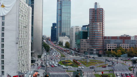 Elevated-footage-of-large-roundabout-circuit-on-multilane-busy-road-in-city-centre.-Tram-standing-inside-intersection.-Tall-modern-buildings-around.-Warsaw,-Poland