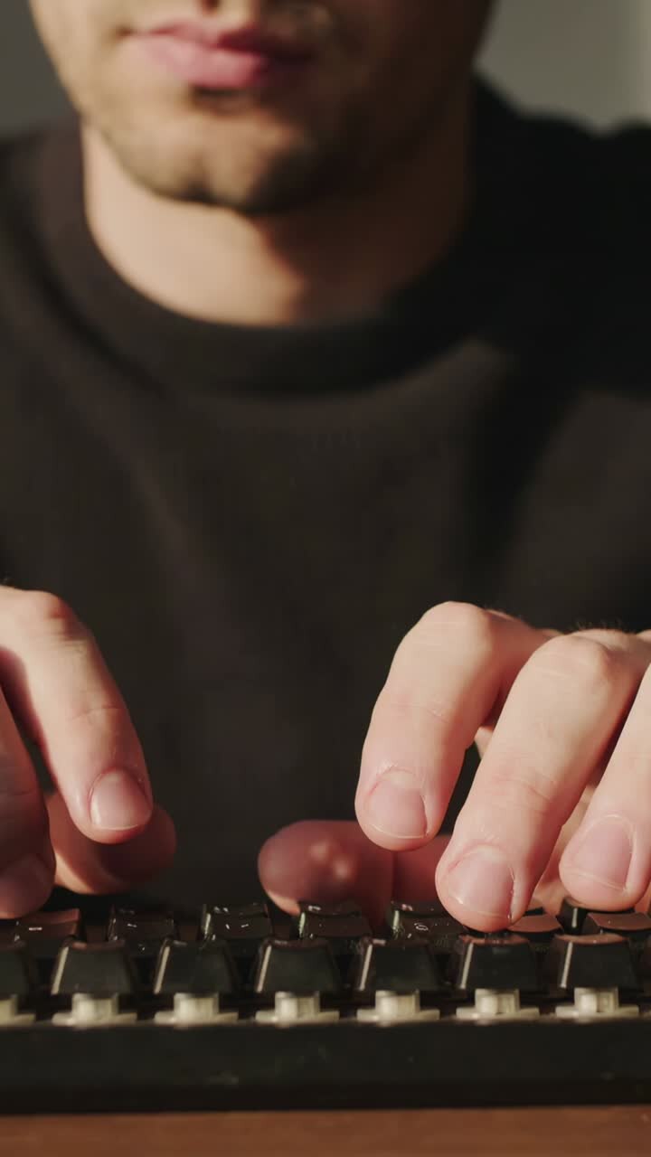 Vertical video: Typing man in dark crewneck hands rising at desk with mechanical keyboard for work