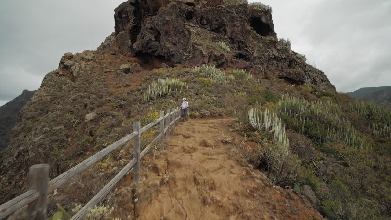 스페인 테네리페에 있는 아나가 산맥의 산등성이에서 전망을 즐기는 여성 등산객을 향해 걷고 있습니다.