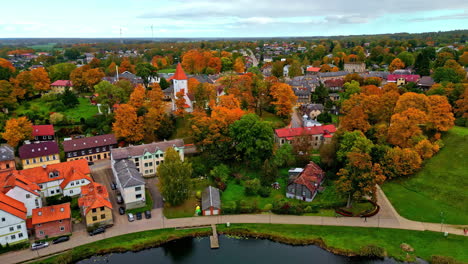 aerial of talsi lake promenade with maple trees surrounding talsi church on an overcast, autumn day
