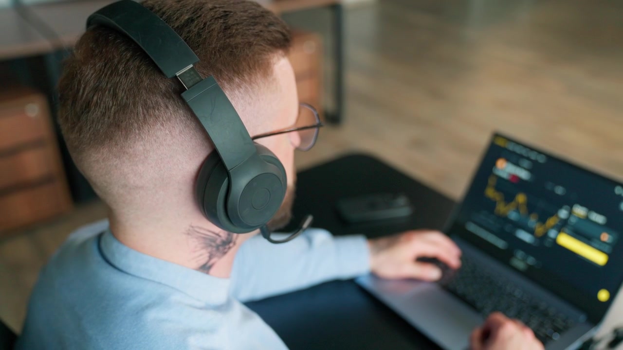 Man in Headphones Working on Laptop with Financial Charts