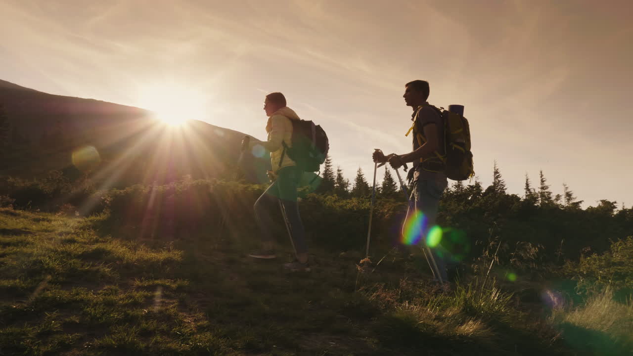 un par de viajeros sube las siluetas de una montaña en los rayos del sol poniente