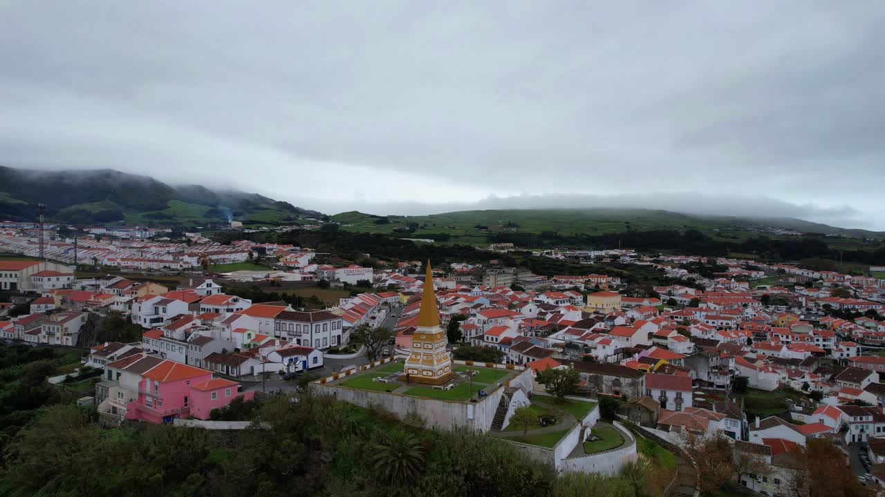 drone sobre el obelisco do alto da memoria en angra, las montañas volcánicas de niebla se vislumbran