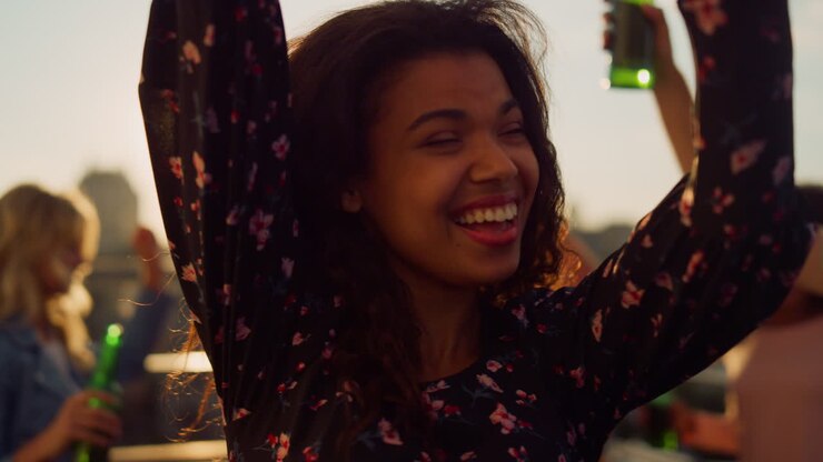 Cheerful afro woman drinking beer at party. African girl dancing outdoors.