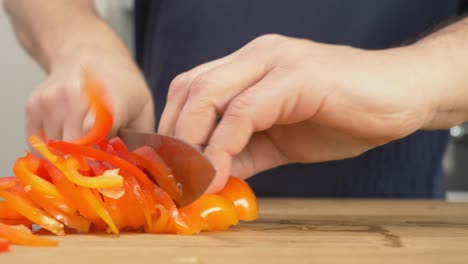 slicing red peppers on a wooden table top with a chef's knife