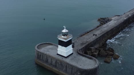 Holyhead-breakwater-lighthouse-longest-concrete-coastal-sea-protection-landmark-aerial-view-slow-orbit-right-with-crashing-waves