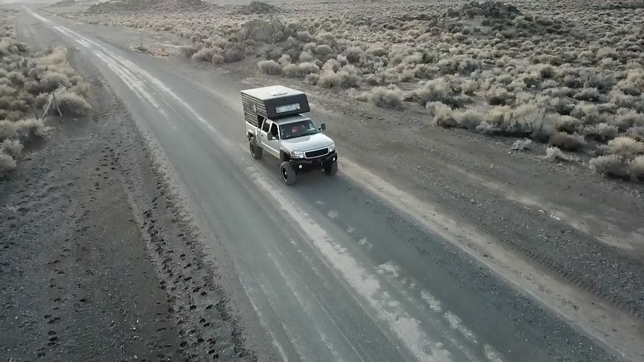 Camión conduciendo por un camino de tierra en el desierto, toma aérea amplia de seguimiento