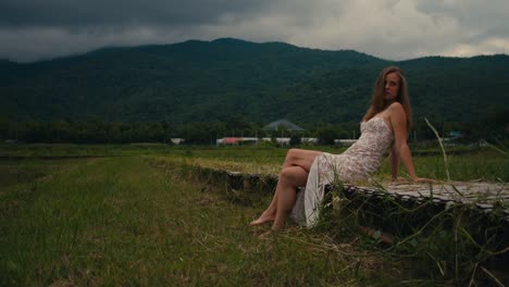 woman in a floral dress sitting on a wooden walkway in a rice field