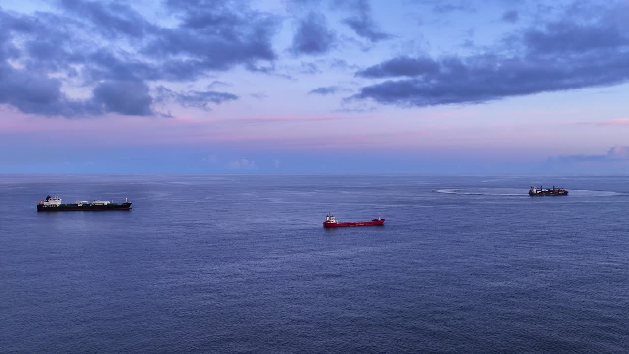 Blue hour arcing aerial view of three anchored freighters in open ocean