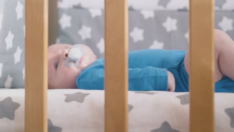 small boy rests with dummy in wooden crib with textile