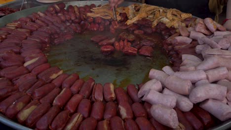 hand flipping chorizo sausages on huge street vendor frying pan, closeup slowmo