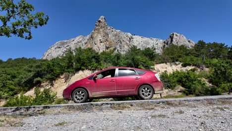 a red car is parked on the side of a winding road with a mountain in the background