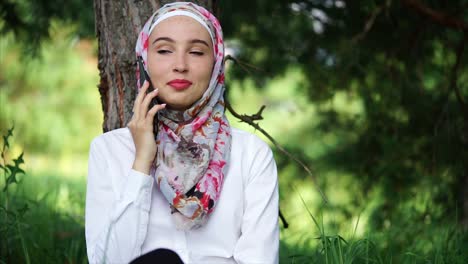 young woman in hijab talking on phone in a park