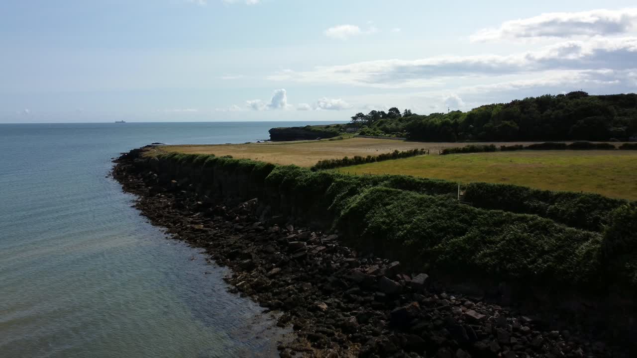 Traeth Lligwy, idilliaco litorale roccioso, vista aerea di un pascolo verde al margine di scogliere rocciose, con ripresa all'indietro.