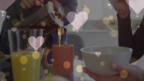 animation of hearts over caucasian female couple eating breakfast