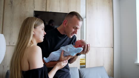 loving parents holding their adorable newborn. father waves a tiny son touching him nose to nose. mother stands close watching.