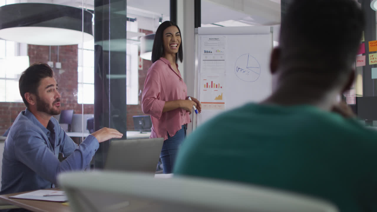 Happy mixed race businesswoman standing near white board having presentation in front of colleuagues