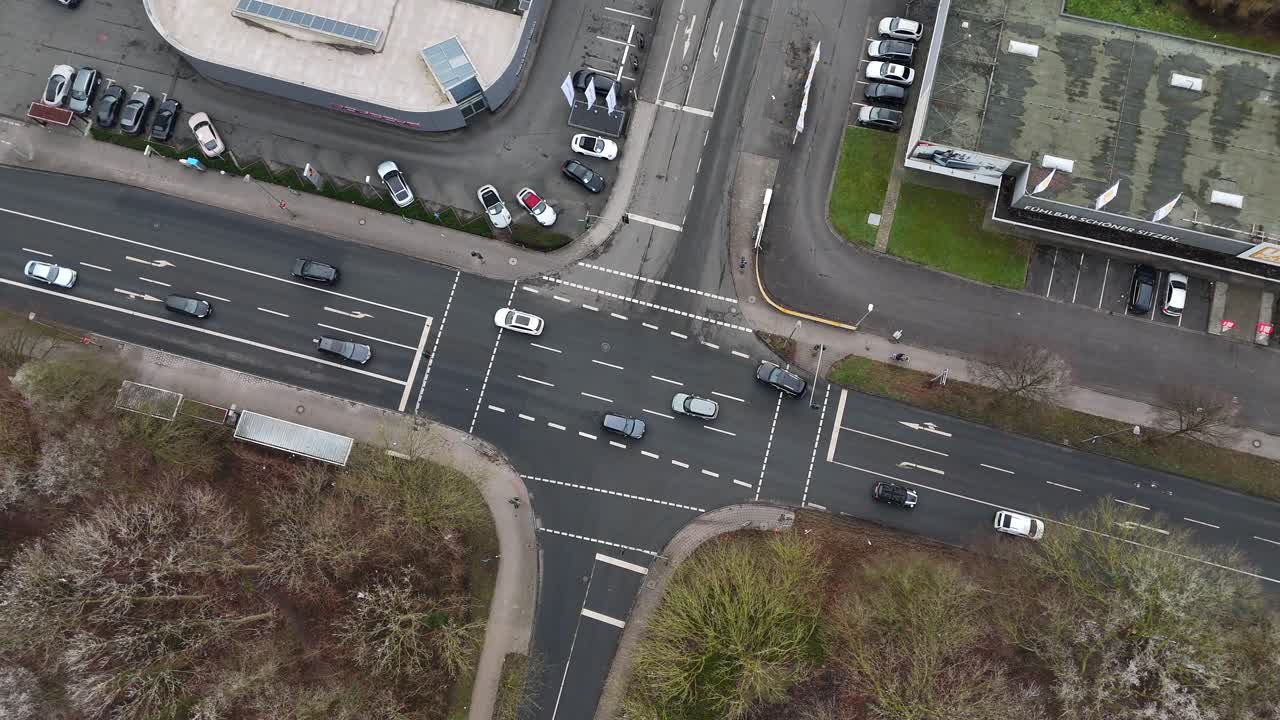 Traffic on main street junction of german town at Porsche Car Dealership store during winter season. Leafless trees in Suburbia. Aerial top down rising shot.
