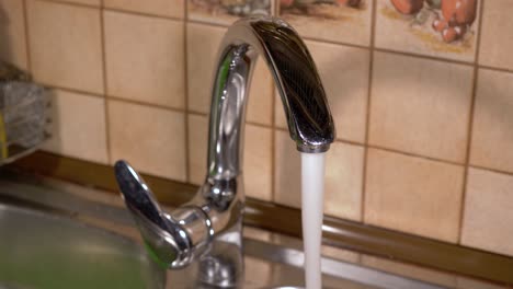 pouring tap water from a faucet in home kitchens sink