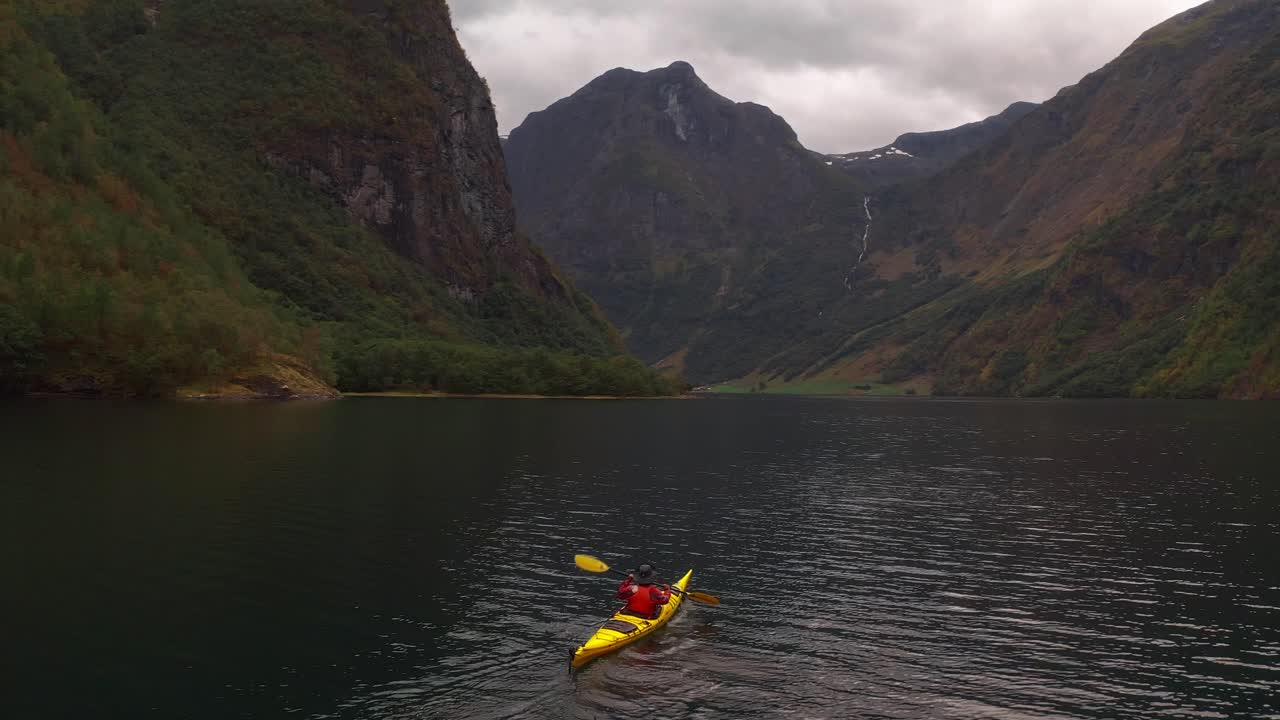 Kayaker paddling through a serene Norwegian fjord surrounded by mountains
