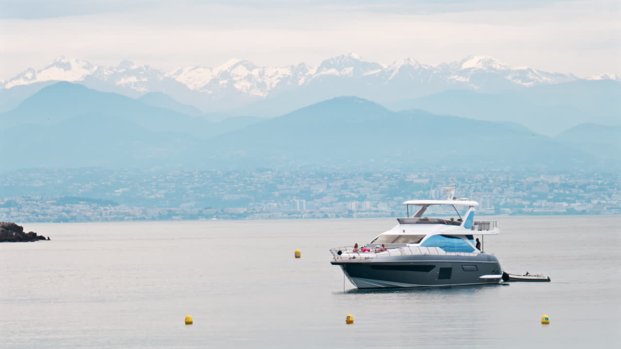 Antibes, France - May 6, 2025: People on a boat docked on the sea with the city and mountains on the background in daylight