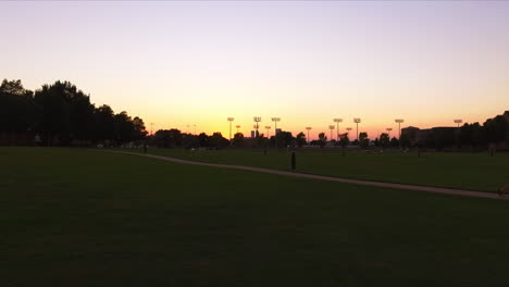 Low-Aerial-Dolly-Vorwärts-Mit-Lebendigem-Sonnenuntergang-Von-Flutlichtern-In-Einem-Park