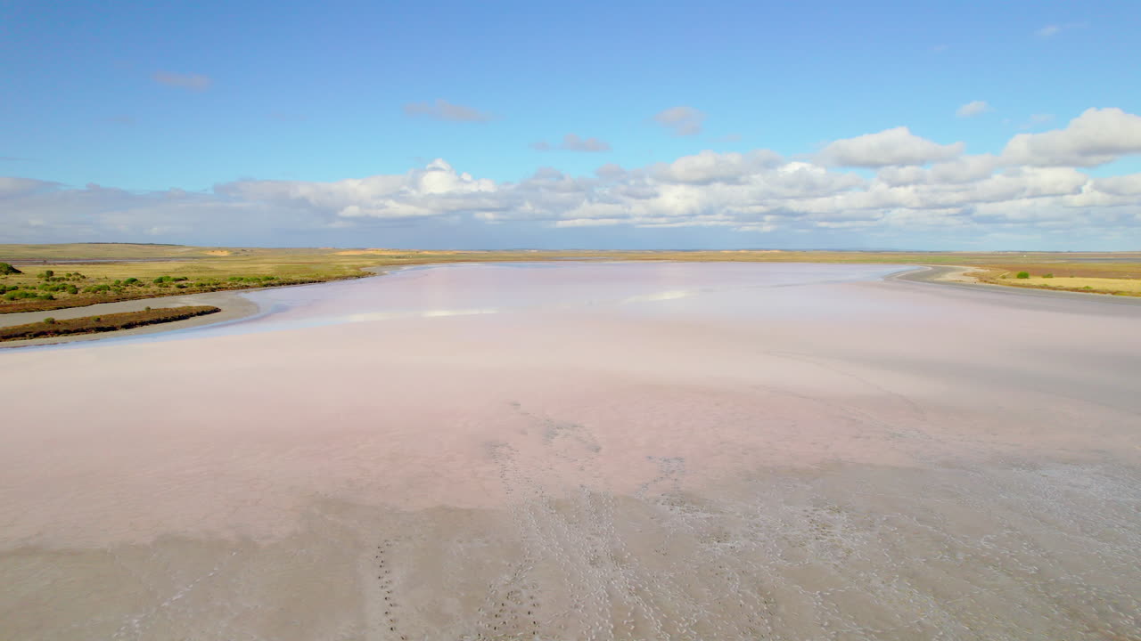 Cinematic aerial pass over a salt lake showing gentle pastel pink shades across the surface. Subtle textures and natural patterns create a soft, abstract and expansive landscape