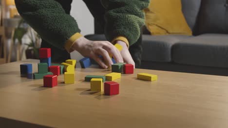 Person-Tidying-Colourful-Wooden-Building-Blocks-From-Table-At-Home-For-Learning-And-Child-Diagnosed-With-ASD