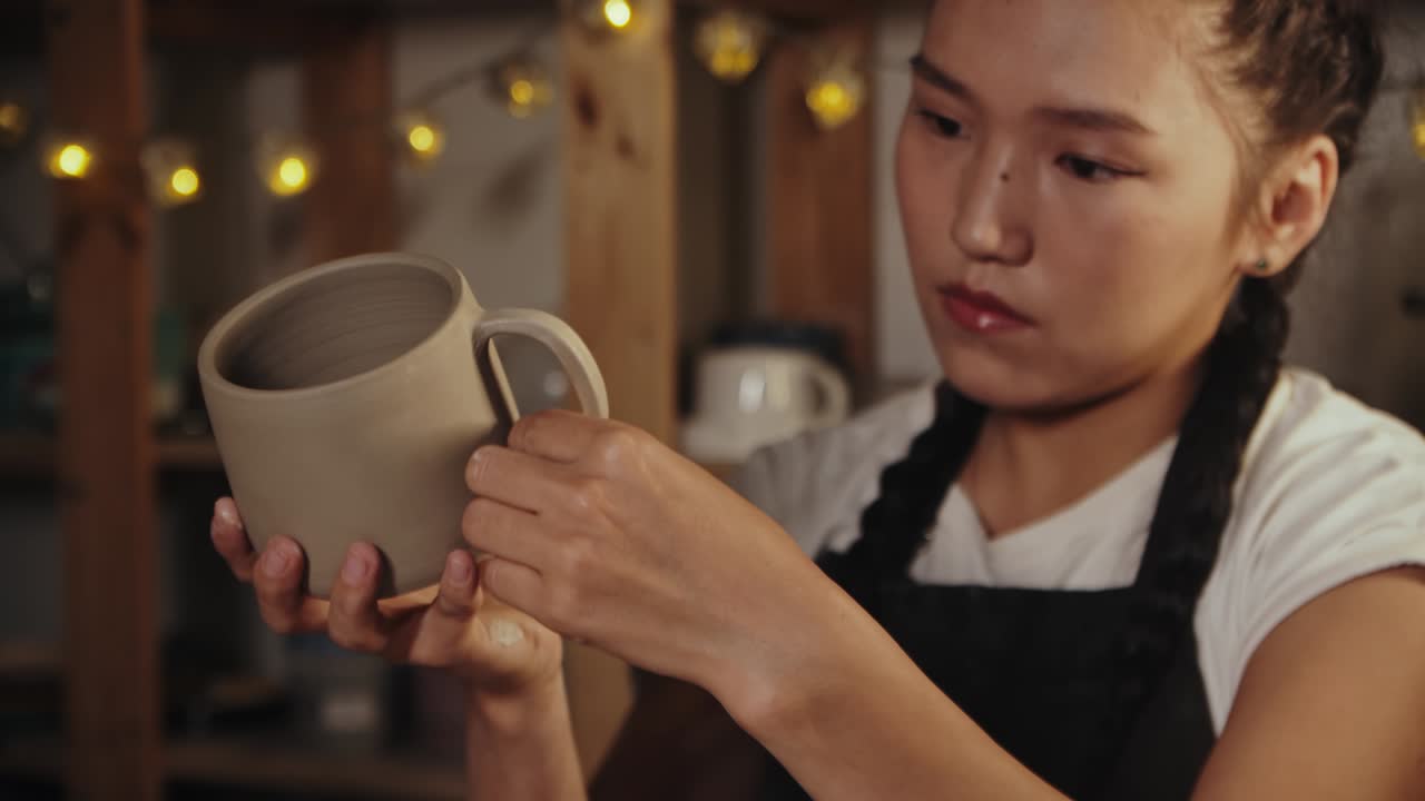 노란색 은 스폰지를 사용하여 점토 컵을 매끄럽게하는 젊은 여성 도자기