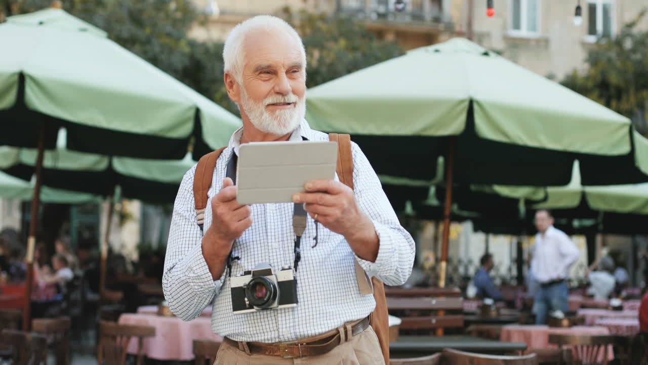 foto de retrato de un alegre turista senior con una cámara fotográfica parada en la terraza del café y teniendo videochat en la tableta