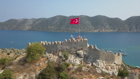 aerial orbits simena castle ruin on rock hilltop flying flag of turkey