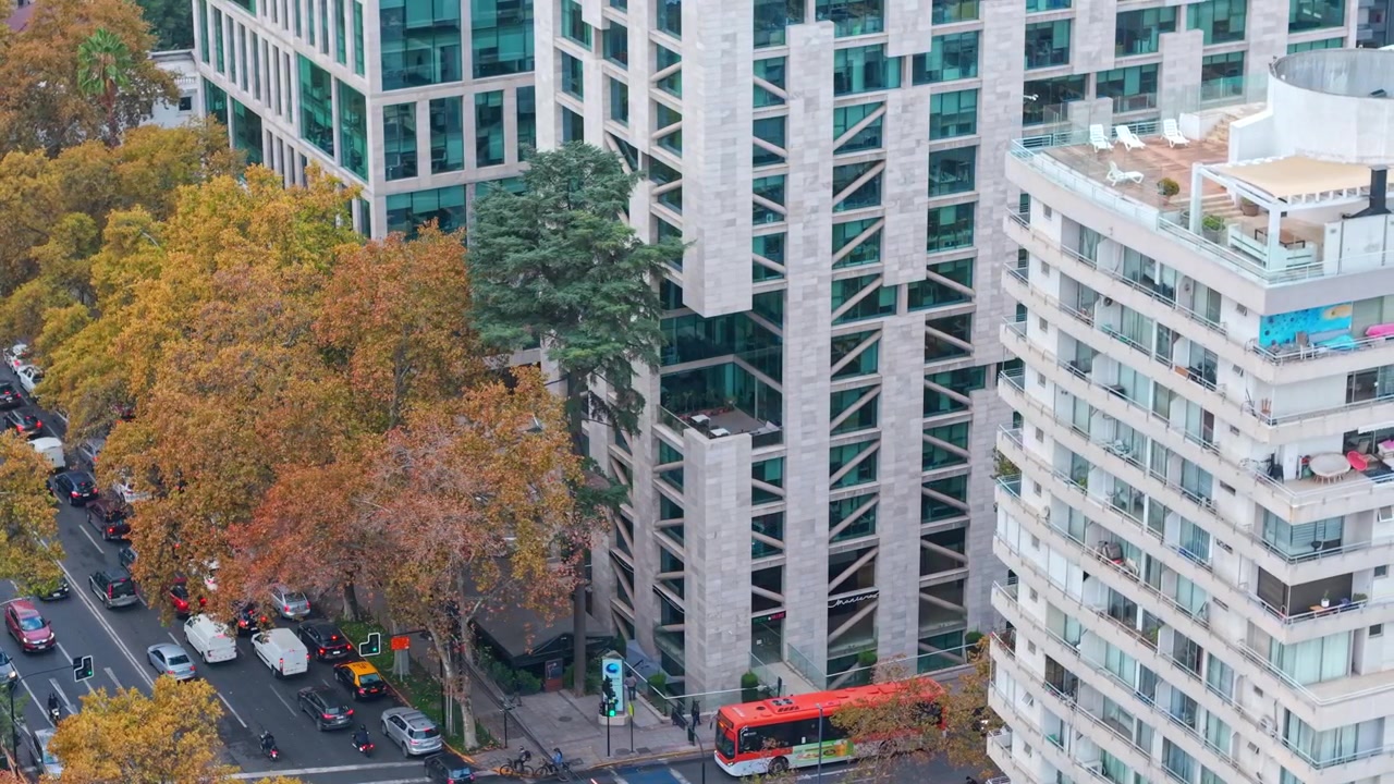 Orbita aerea con teleobiettivo di un moderno edificio per uffici con un balcone a metà altezza a Providencia, Santiago, Cile, in una giornata di sole con traffico intenso.