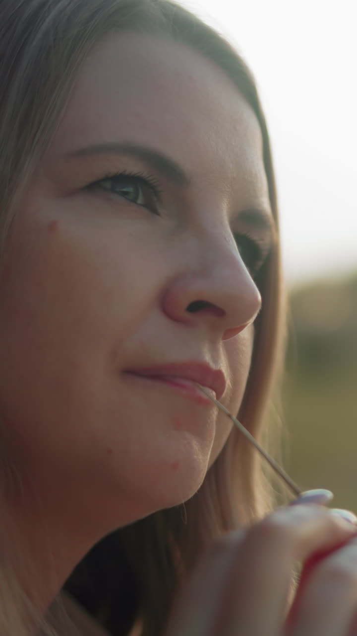 primer plano de una mujer de negocios perdida en sus pensamientos, girando suavemente un hilo de heno en los dedos, la cálida luz dorada del sol destaca su expresión contemplativa, con un fondo de campo borroso