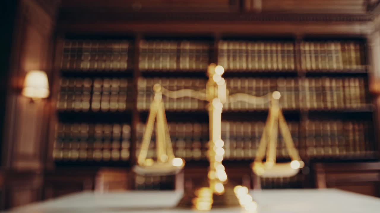 Low-angle video shot of golden scales of justice on a marble table, with a blurred background of law